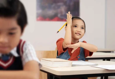 asian-schoolgirl-sitting-desk-classroom-lifting-up-her-hand-answer_11zon